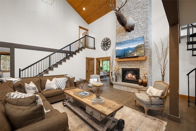 Living room featuring stairs, wood finished floors, high vaulted ceiling, a stone fireplace, and recessed lighting