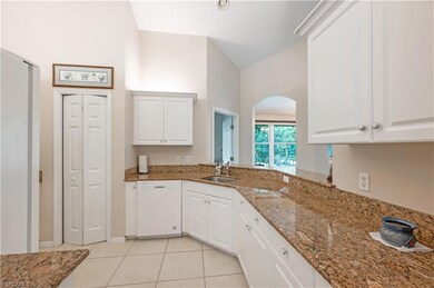 Kitchen featuring white dishwasher, light tile patterned floors, white cabinets, lofted ceiling, and stone countertops