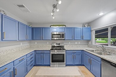 Kitchen with blue cabinets, stainless steel appliances, light wood-type flooring, and light stone counters