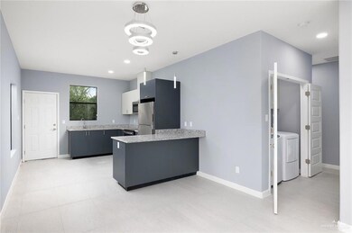 Kitchen featuring appliances with stainless steel finishes, washing machine and dryer, kitchen peninsula, white cabinetry, and decorative light fixtures
