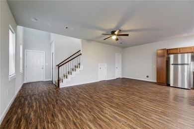 Unfurnished living room with dark wood-type flooring, stairs, and a ceiling fan