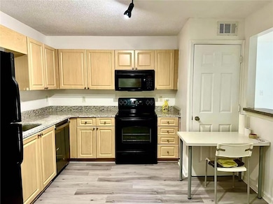 Kitchen featuring light brown cabinets, black appliances, a textured ceiling, light wood-type flooring, and light stone countertops