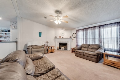 Living area with carpet, a tiled fireplace, ceiling fan, and a textured ceiling