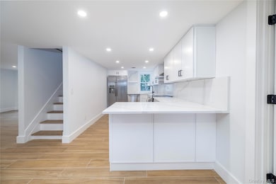 Kitchen with wood finish floors, light stone countertops, recessed lighting, appliances with stainless steel finishes, and white cabinetry