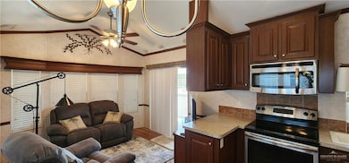 Kitchen featuring dark brown cabinets, vaulted ceiling, appliances with stainless steel finishes, ceiling fan, and open floor plan