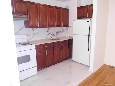 Kitchen featuring white appliances, tasteful backsplash, under cabinet range hood, light marble finish floors, and light stone countertops