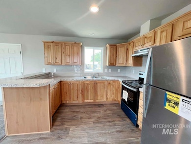 Kitchen with freestanding refrigerator, black / electric stove, light brown cabinetry, a peninsula, and recessed lighting