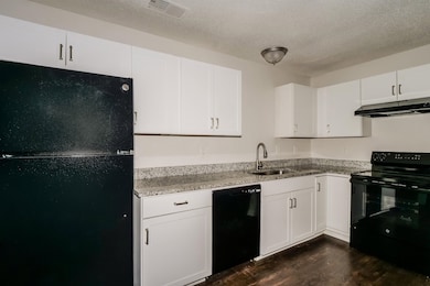 Kitchen with black appliances, light stone counters, a textured ceiling, white cabinets, and dark wood-style floors