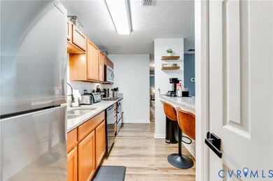 Kitchen with stainless steel appliances, light wood-style floors, light stone countertops, a textured ceiling, and a kitchen bar
