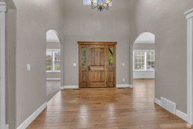 Entryway with a high ceiling, light wood finished floors, arched walkways, and a chandelier