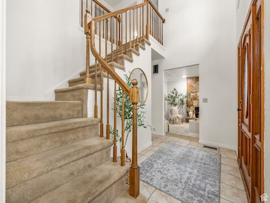 Foyer featuring a stone fireplace, tile patterned flooring, a high ceiling, and stairs