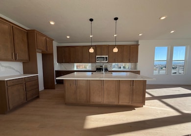 Kitchen featuring brown cabinets, pendant lighting, an island with sink, light wood-style floors, and light stone counters