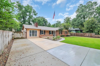 Ranch-style home featuring a chimney, concrete driveway, brick siding, roof with shingles, and view of scattered trees