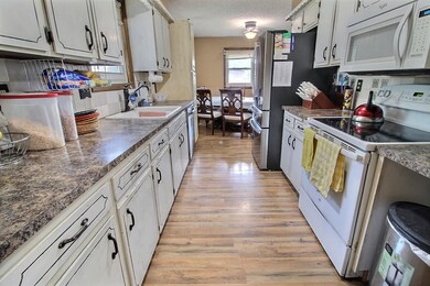 Kitchen with white appliances, light wood-style floors, a textured ceiling, and dark countertops