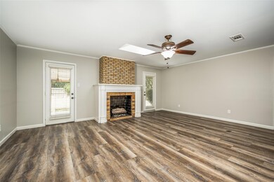 Unfurnished living room with a skylight, ceiling fan, a brick fireplace, brick wall, and wood-type flooring