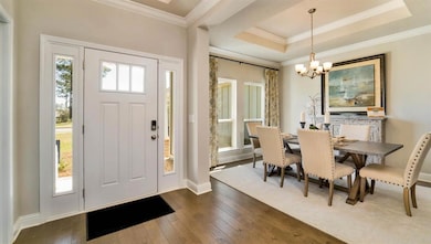 Foyer entrance with ornamental molding, dark wood-style floors, a chandelier, and a tray ceiling