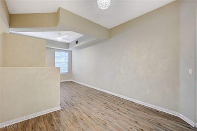 Unfurnished room featuring a tray ceiling, visible vents, a ceiling fan, wood finished floors, and baseboards