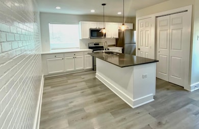 Kitchen with white cabinetry, appliances with stainless steel finishes, an island with sink, light wood-style floors, and recessed lighting