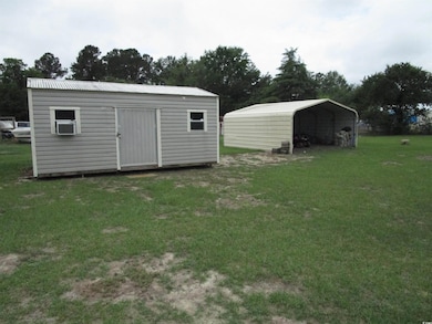 View of shed with a carport, cooling unit, and view of wooded area