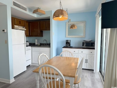 Kitchen with white appliances, light wood-style flooring, dark countertops, and under cabinet range hood