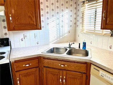 Kitchen featuring electric range oven, white dishwasher, brown cabinets, light countertops, and tasteful backsplash