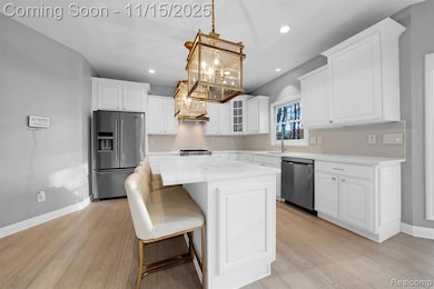 Kitchen with white cabinets, glass insert cabinets, stainless steel appliances, a breakfast bar area, and light wood finished floors
