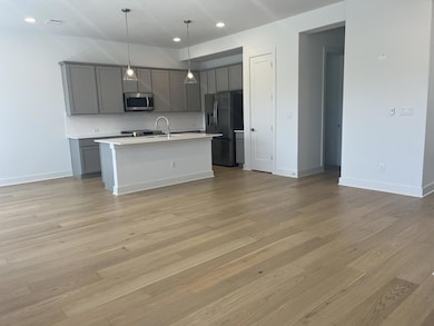 Kitchen featuring gray cabinetry, hanging light fixtures, stainless steel appliances, an island with sink, and recessed lighting