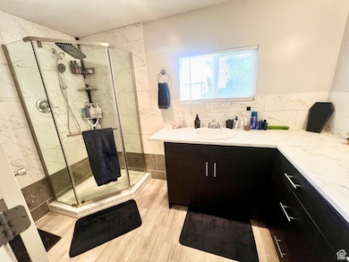 Full bathroom with vanity, a marble finish shower, light wood-style flooring, and backsplash