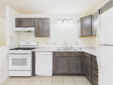 Kitchen with white appliances, dark brown cabinetry, light countertops, light tile patterned flooring, and a textured ceiling