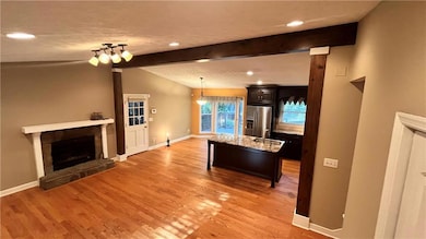 Kitchen with a kitchen breakfast bar, an island with sink, open floor plan, a tile fireplace, and light stone counters