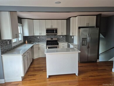 Kitchen featuring white cabinetry, appliances with stainless steel finishes, a kitchen island, tasteful backsplash, and light stone counters