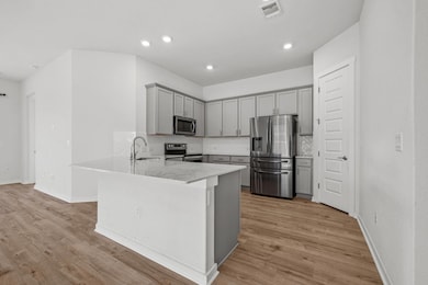 Kitchen with gray cabinets, appliances with stainless steel finishes, a peninsula, tasteful backsplash, and light wood-type flooring