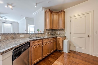 Kitchen featuring stainless steel dishwasher, a sink, brown cabinetry, dark wood-style floors, and crown molding