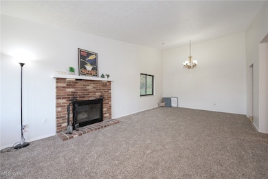 Unfurnished living room featuring a brick fireplace, carpet flooring, and a chandelier