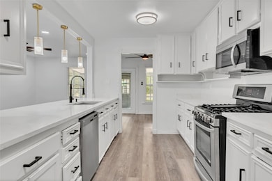 Kitchen featuring appliances with stainless steel finishes, hanging light fixtures, white cabinets, light wood-style floors, and recessed lighting