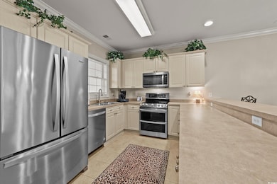 Kitchen featuring appliances with stainless steel finishes, ornamental molding, light countertops, light tile patterned floors, and a sink