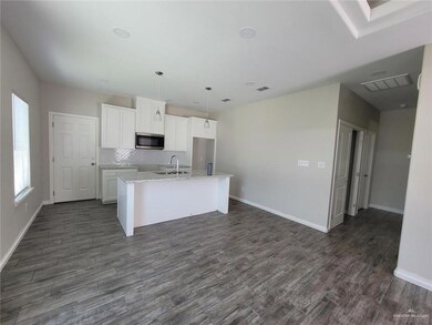 Kitchen featuring dark wood-type flooring, sink, white cabinetry, an island with sink, and pendant lighting