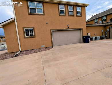Rear view of property featuring an attached garage, driveway, and stucco siding