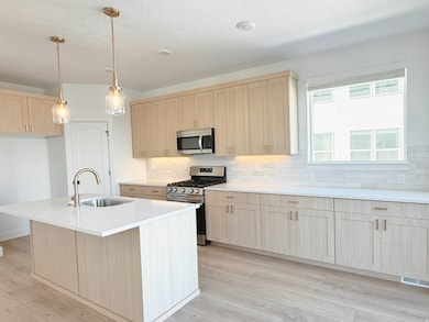 Kitchen featuring light brown cabinetry, stainless steel appliances, light wood-style floors, backsplash, and a center island with sink