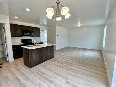 Kitchen with black appliances, a sink, baseboards, light countertops, and a kitchen island with sink