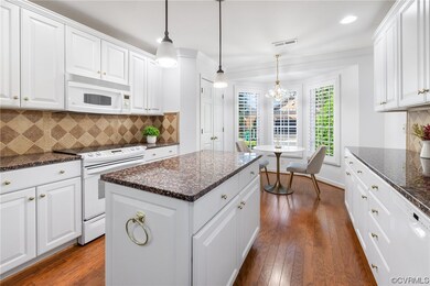 Kitchen featuring a kitchen island with sink, crown molding, decorative light fixtures, dark stone counters, white cabinets, white appliances, backsplash, and light hardwood floors