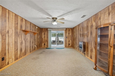 Unfurnished living room with a textured ceiling, carpet, ceiling fan, wood walls, and heating unit