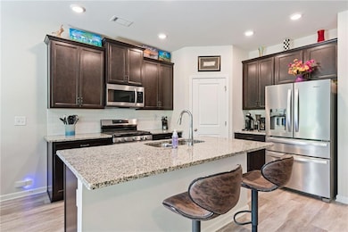 Kitchen featuring appliances with stainless steel finishes, light wood finished floors, dark brown cabinetry, and recessed lighting