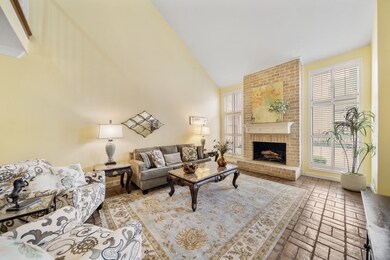 A cozy brick surrounded wood burning fireplace with custom mantel & bricked heart is flanked by floor-to-ceiling windows with plantation shutters.