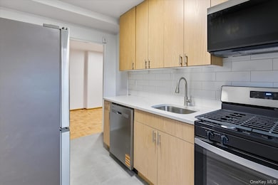 Kitchen featuring light brown cabinets, stainless steel appliances, light stone counters, and backsplash