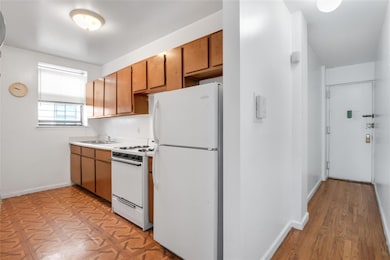 Kitchen with white appliances, baseboards, a sink, light countertops, and brown cabinets
