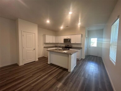 Kitchen featuring stainless steel appliances, a center island with sink, light stone countertops, dark wood-type flooring, and white cabinets