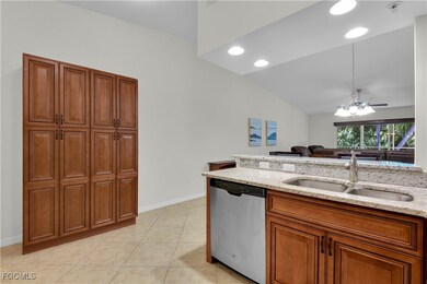 Kitchen with brown cabinetry, stainless steel dishwasher, recessed lighting, light stone countertops, and vaulted ceiling
