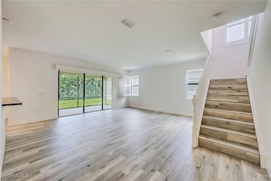 Unfurnished living room featuring stairs and light wood-style floors