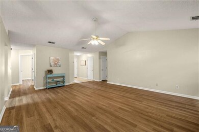 Unfurnished living room with ceiling fan, wood finished floors, lofted ceiling, and a textured ceiling